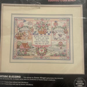 May include: A framed Dimensions counted cross stitch kit. The design features a pastoral scene with houses, flowers, rabbits, sheep, and the text "Father, hear and bless the beasts and singing birds... Guard with tenderness small things that have no words."