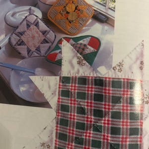 Może przedstawiać: Kolekcja kwadratowych pikowanych łapek kuchennych z wzorami gwiazd w r&oacute;żnych kolorach, w tym czerwone, zielone, białe i pomarańczowe wzory w kratę oraz kwiatowe. Łapki są prezentowane obok białego czajnika, miski z jajkami i miski do mieszania.