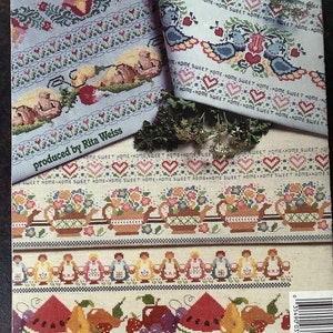 Può includere: Un libro di schemi per punto croce con vari disegni. La copertina presenta bordi dettagliati a punto croce con motivi floreali, di frutta e uccelli. Il testo "HOME SWEET HOME" è ripetuto. Prodotto da Rita Weiss.