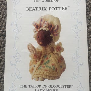 Puede incluir: Portada de libro con una Lady Mouse tejida de "The Tailor of Gloucester" de Beatrix Potter. El ratón lleva un vestido y un gorro amarillos. El título "The World of Beatrix Potter" está en la parte superior.