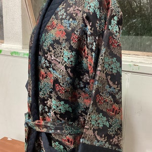 May include: A black silk robe with a quilted collar and cuffs. The robe features a colorful floral and landscape pattern with gold accents.