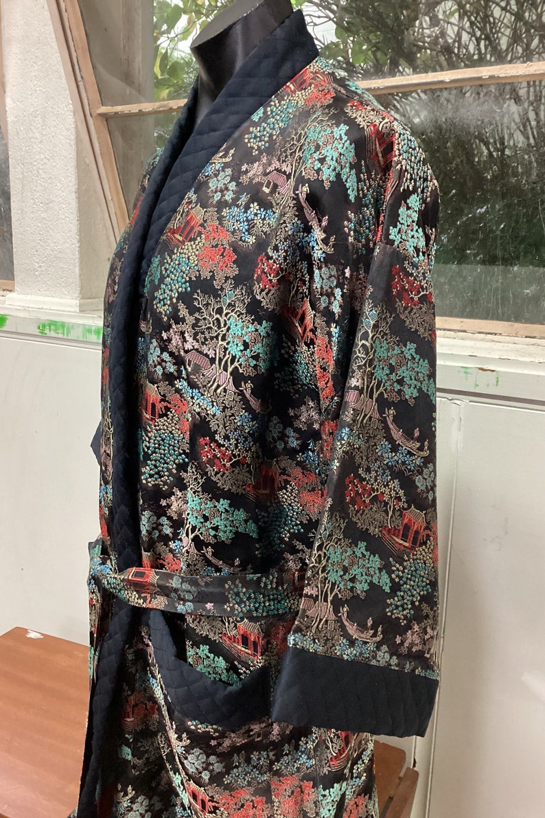 May include: A black silk robe with a quilted collar and cuffs. The robe features a colorful floral and landscape pattern with gold accents.
