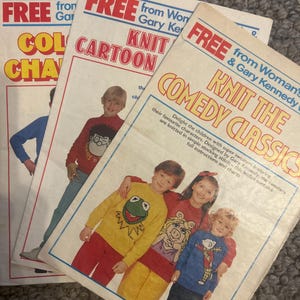 May include: Three vintage knitting pattern leaflets featuring children wearing sweaters with cartoon characters. The top leaflet is titled Knit The Comedy Classics and shows children in yellow, red, and blue sweaters with Kermit and Miss Piggy designs.