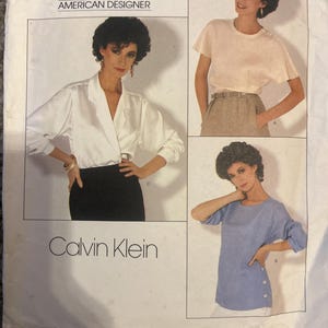 May include: Vogue Patterns sewing pattern featuring Calvin Klein designs. The pattern includes images of a woman wearing a white wrap blouse, a light-colored t-shirt, and a blue top with side buttons. The pattern number is 1128.