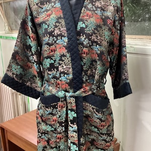 May include: A black silk robe with a floral pattern and a black quilted lining. The robe has a sash tie and long sleeves.