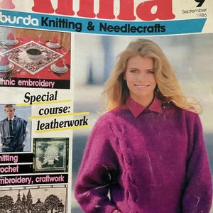 May include: The cover of "Anna" magazine, September 1986 issue, features a woman wearing a magenta cable-knit sweater over a collared shirt. The magazine's title is in large red letters. Other text includes "burda Knitting & Needlecrafts" and "Fashion Knits for Fall".