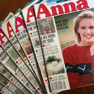May include: A stack of vintage "Anna" knitting and needlecraft magazines. The covers feature images of knitwear, embroidery, and crochet projects. The magazine titles include "Knit & Crochet Sweaters" and "Knit and Crochet Fashion". The magazines are fanned out on a wooden surface.