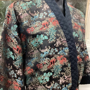 May include: Black silk robe with a quilted black collar and a gold, red, and blue floral pattern. The robe has a sash tie.