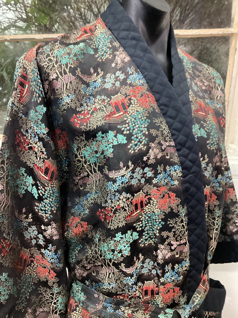 May include: Black silk robe with a quilted black collar and a gold, red, and blue floral pattern. The robe has a sash tie.