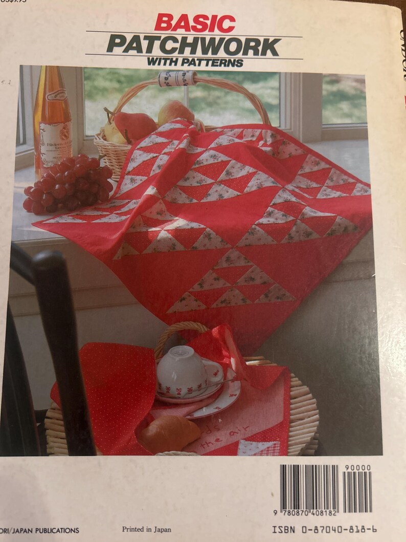Może przedstawiać: Książka pod tytułem Basic Patchwork with Patterns z czerwonobiałym geometrycznym quiltem na okładce. Okładka przedstawia czerwony quilt w tr&oacute;jkątne wzory, kosz z owocami, białą filiżankę na spodku oraz rogalik. ISBN 0-87040-818-6.
