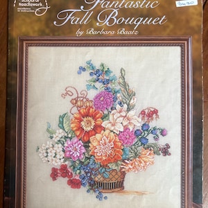 Può includere: Un modello a punto croce intitolato "Fantastic Fall Bouquet" di Barbara Baatz. L'immagine presenta un disegno a punto croce incorniciato di una colorata composizione floreale in un cesto. Il bouquet comprende fiori arancioni, rosa, bianchi e blu.