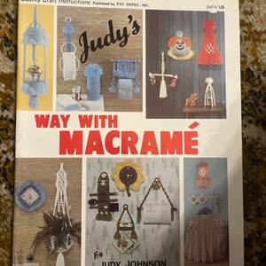May include: A book cover with the title "Judy's Way With Macrame" by Judy Johnson. The cover features a variety of macrame projects, including wall hangings, plant hangers, and a clock.