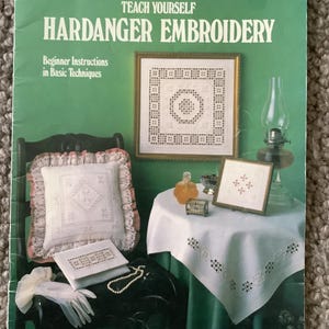 May include: A green leaflet titled "Teach Yourself Hardanger Embroidery" with the Leisure Arts logo. The cover features examples of embroidered pieces, including a framed square and a pillow. The text reads "Beginner Instructions in Basic Techniques."