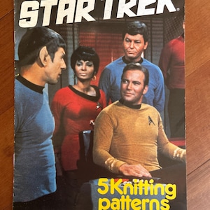 Peut inclure: Un livret de modèles de tricot Star Trek de 1987 avec une photographie en couleur de quatre membres d'équipage en uniformes bleu, rouge et or. Le titre STAR TREK est imprimé en blanc en haut, et 5 Knitting patterns by Gary Kennedy en bas.