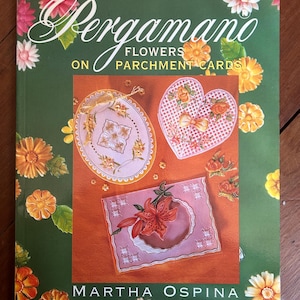 May include: A softcover book titled Pergamano Flowers on Parchment Cards by Martha Ospina. The green cover features illustrations of orange and pink flowers and a central inset showing three handmade parchment cards with floral designs.