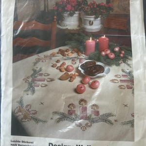 May include: A pre-stamped tablecloth for hand embroidery, featuring a Christmas design. The design includes three candles, greenery, and festive elements. The packaging includes the text "Sarah-Handarbeit" and "Design: Weihnachts-Trio".