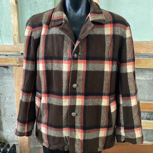 May include: A brown, beige, and orange plaid jacket with a button closure. The jacket has two pockets on the front.