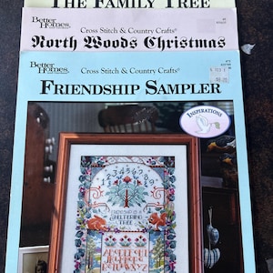 May include: A stack of cross-stitch pattern booklets with titles including "Home for Christmas," "The Family Tree," "North Woods Christmas," and "Friendship Sampler." The "Friendship Sampler" booklet features a framed cross-stitch design with a tree and alphabet.