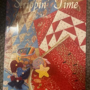 May include: A craft pattern book titled Strippin' Time Project of the Month by J. Jane Mitchell and Patsy Padgett. The cover features a colorful quilt design with blue, red, and white fabric patterns, a small basket of thread, and fabric shapes.