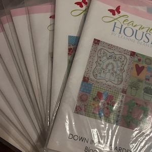 May include: A stack of multiple identical sewing pattern booklets in clear plastic sleeves. The cover features a red butterfly logo, the text Leanne House by Leanne Beasley, and a quilt block design titled Down in the Garden Block One.