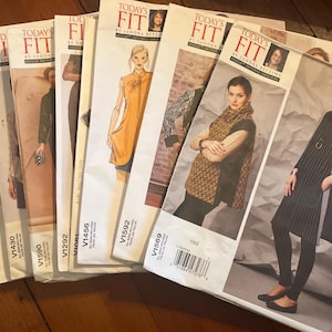 May include: A collection of Today's Fit by Sandra Betzina Vogue sewing patterns arranged in a fan shape. Each white paper envelope features a photograph of a garment, the pattern number, and the brand logo. The patterns include V1574, V1430, V1590, V1292, V1456, V1592, and V1569.