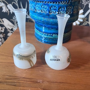 Puede incluir: Dos jarrones de cristal esmerilado con detalles pintados en oro y marrón. Los jarrones tienen una base bulbosa y un cuello delgado. El fondo incluye un jarrón de cerámica azul y papel pintado estampado.