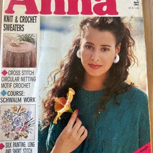 May include: A vintage magazine cover titled "Anna" features a woman wearing a teal sweater and holding a yellow flower. The cover includes text about knitting, crochet, cross stitch, and silk painting. The magazine is dated April 1991.