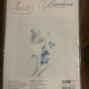 May include: A cross-stitch embroidery kit by Luca-S titled Summer delight, featuring a butterfly and blue bell flowers. The packaging includes the text 82248, Dim.: 20x28 cm, and Alda: 16. The design is printed on a white background inside a clear plastic bag.