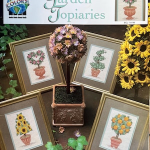 Può includere: Un libro di schemi per punto croce intitolato "Garden Topiaries" con disegni ricamati incorniciati di piante in vaso, tra cui girasoli, rose e alberi di arance. La copertina mostra il logo True Colors Cross Stitch e il testo "Garden Topiaries".