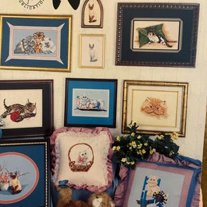 Puede incluir: Una colección de arte de punto de cruz enmarcados con varios retratos de gatos. La obra de arte incluye imágenes de gatitos, gatos en cestas y otros diseños con temática felina. La palabra "Kittens" se muestra en la parte superior de la imagen.