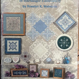 Könnte beinhalten: Ein Softcover-Buch mit dem Titel Elegant Accents II In Hardanger Embroidery von Rosalyn K. Watnemo. Das Cover zeigt eine Collage verschiedener Hardanger-Stickereiprojekte, darunter gerahmte Stücke, Deckchen und kleine Dekorationsartikel in Blau-, Weiß- und Neutraltönen.