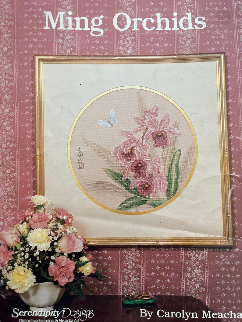 Pode incluir: Obra de arte emoldurada intitulada "Ming Orchids" com um design circular de orqu&iacute;deas rosa e uma borboleta. A obra de arte com moldura dourada est&aacute; sobre um papel de parede floral rosa. Um buqu&ecirc; de flores est&aacute; em frente &agrave; obra de arte.