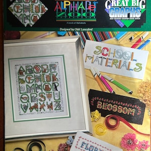 May include: A softcover book titled Alphabet Zoo and Great Big Graphs featuring counted cross stitch patterns. The cover displays a framed animal alphabet sampler, embroidered text reading School Materials, Blossom, and Florals, and colourful craft supplies.