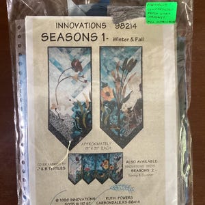 Könnte beinhalten: Ein teilweise fertiggestelltes Patchwork-Hängekit mit dem Titel "Innovations 98214 Seasons 1 - Winter & Fall". Das Kit enthält zwei Paneele, jedes etwa 33 cm x 79 cm groß, mit einer Winter- und einer Herbstlandschaft. Das Kit wird von Innovations hergestellt und von Ruth Powers entworfen.