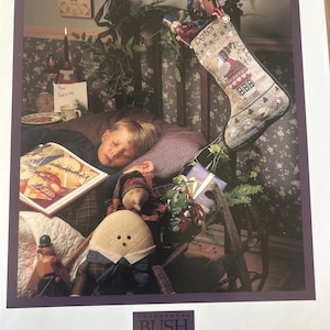 Può includere: Immagine stampata di una scena natalizia con una calza a punto croce con l'etichetta "Peter's Stocking". L'immagine include un bambino che dorme, una bambola e una scena natalizia con un orologio e una candela.