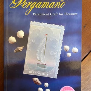 May include: A book titled Pergamano Parchment Craft for Pleasure by Pat Hosking. The dark blue cover features a central illustration of a sailboat on a card with the text BEST WISHES, surrounded by various seashells and a small pink fan logo.