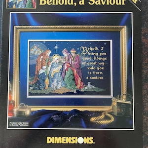 Könnte beinhalten: Ein Dimensions Kreuzstich-Set mit dem Titel "Behold, a Saviour" von Linda Green. Das Set zeigt ein gerahmtes Kreuzstich-Design, das die Weihnachtsgeschichte mit dem Text "Behold, I bring you good tidings of great joy... unto you is born a saviour." darstellt.
