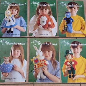 May include: A collection of six Alice in Wonderland craft pattern booklets featuring plush toys including Alice, a Cheshire Cat, a blue caterpillar, a dormouse in a teapot, a white rabbit with a heart banner, and a Mad Hatter doll.