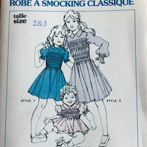 May include: A vintage sewing pattern for a classic yoke dress, featuring three different styles. The illustration shows three children's dresses in blue and pink, with the text "CLASSIC YOKE DRESS" and "GRACE L. KNOTT SMOCKING SUPPLIES LTD."