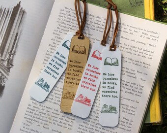 May include: Four colourful bookmarks with a stack of books illustration and the text "We lose ourselves in books, we find ourselves there too."  The bookmarks are made of different materials, including wood and paper.