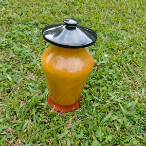 May include: A wooden urn with a black lid, sitting on a bed of green grass.