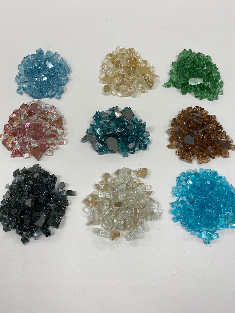 May include: Nine piles of different coloured glass fire pit stones. The colours are blue, beige, green, pink, teal, brown, grey, clear, and light blue.