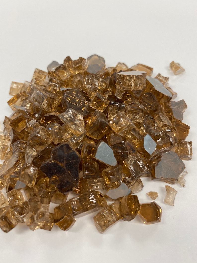 May include: A pile of small, translucent brown glass pieces. The glass pieces are irregular in shape and size, with some having a slightly iridescent sheen.
