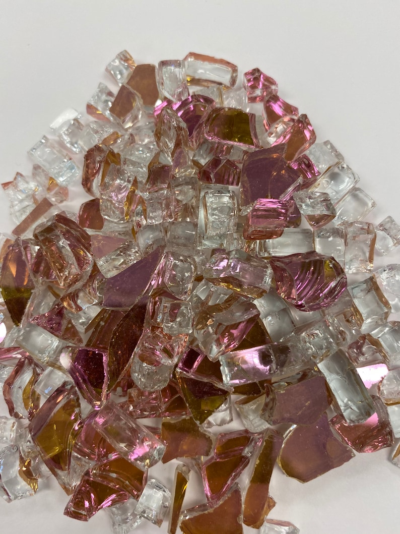 May include: A pile of iridescent glass pieces in shades of pink, gold, and clear. The glass pieces are irregular in shape and size, and they have a reflective surface.