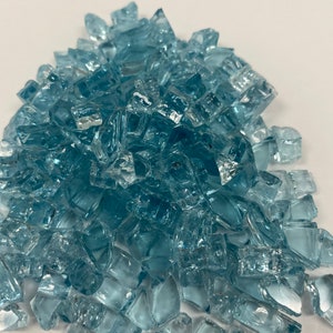 May include: A pile of light blue glass pieces, likely for use in a fire pit or decorative landscaping.