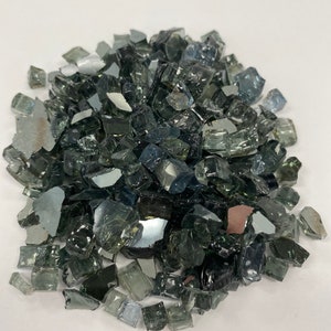 May include: A pile of small, dark grey and clear glass pieces. The glass pieces are irregular in shape and size, and they have a reflective surface.