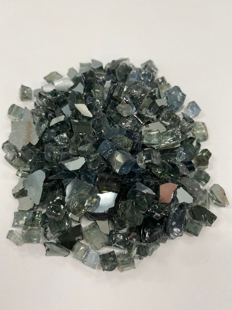 May include: A pile of small, dark grey and clear glass pieces. The glass pieces are irregular in shape and size, and they have a reflective surface.