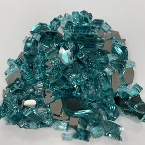 May include: A pile of teal blue and silver glass fire pit gems. The glass pieces are various sizes and shapes.