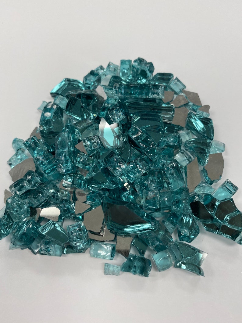 May include: A pile of teal blue and silver glass fire pit gems. The glass pieces are various sizes and shapes.