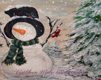 May include: A snowman wearing a black top hat and a green scarf stands in a snowy winter scene. A red cardinal perches on a branch of a snow-covered evergreen tree.